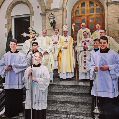 Priesterweihe P. Kulla, Gruppenbild vor der Klosterpforte mit Bischof, Neupriester, Konzelebranten und Ministrant*innen