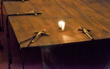 Kreuze, die auf einem Tisch um eine Kerze gruppiert liegen.